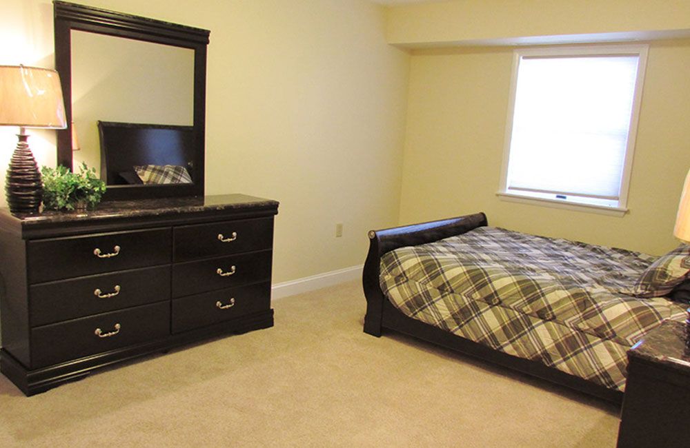 A neatly arranged bedroom with a bed, dresser, and window.