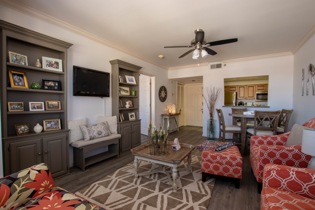 A cozy living room with modern decor, featuring a ceiling fan, bookshelf, and wood flooring.