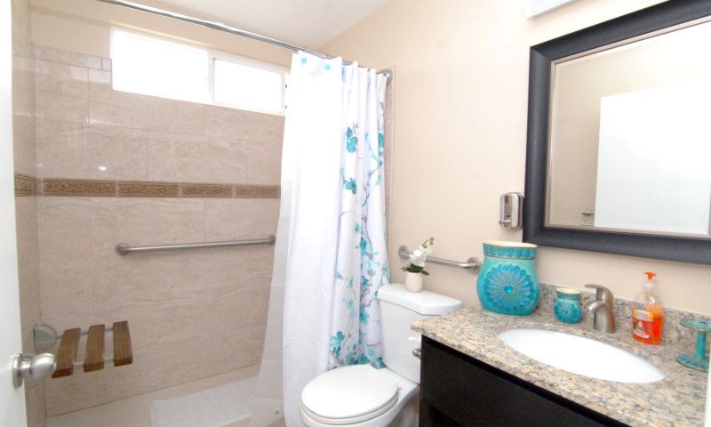 A modern bathroom featuring a shower with a floral curtain, toilet, countertop with sink, and mirror. Decor includes turquoise accents.