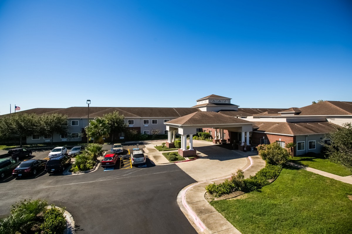 A spacious building with a parking lot and landscaped entrance under a clear blue sky.