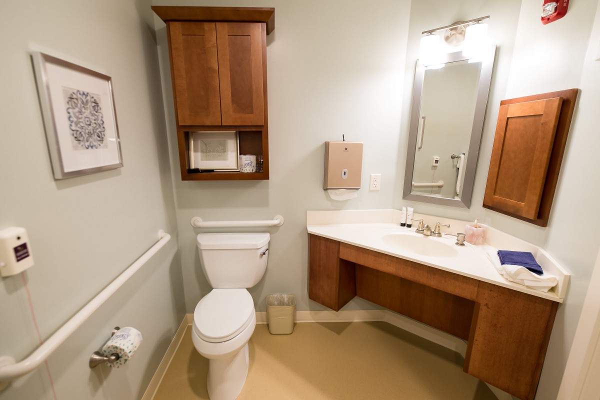 A clean and functional bathroom with a toilet, sink, mirror, and wooden cabinetry.