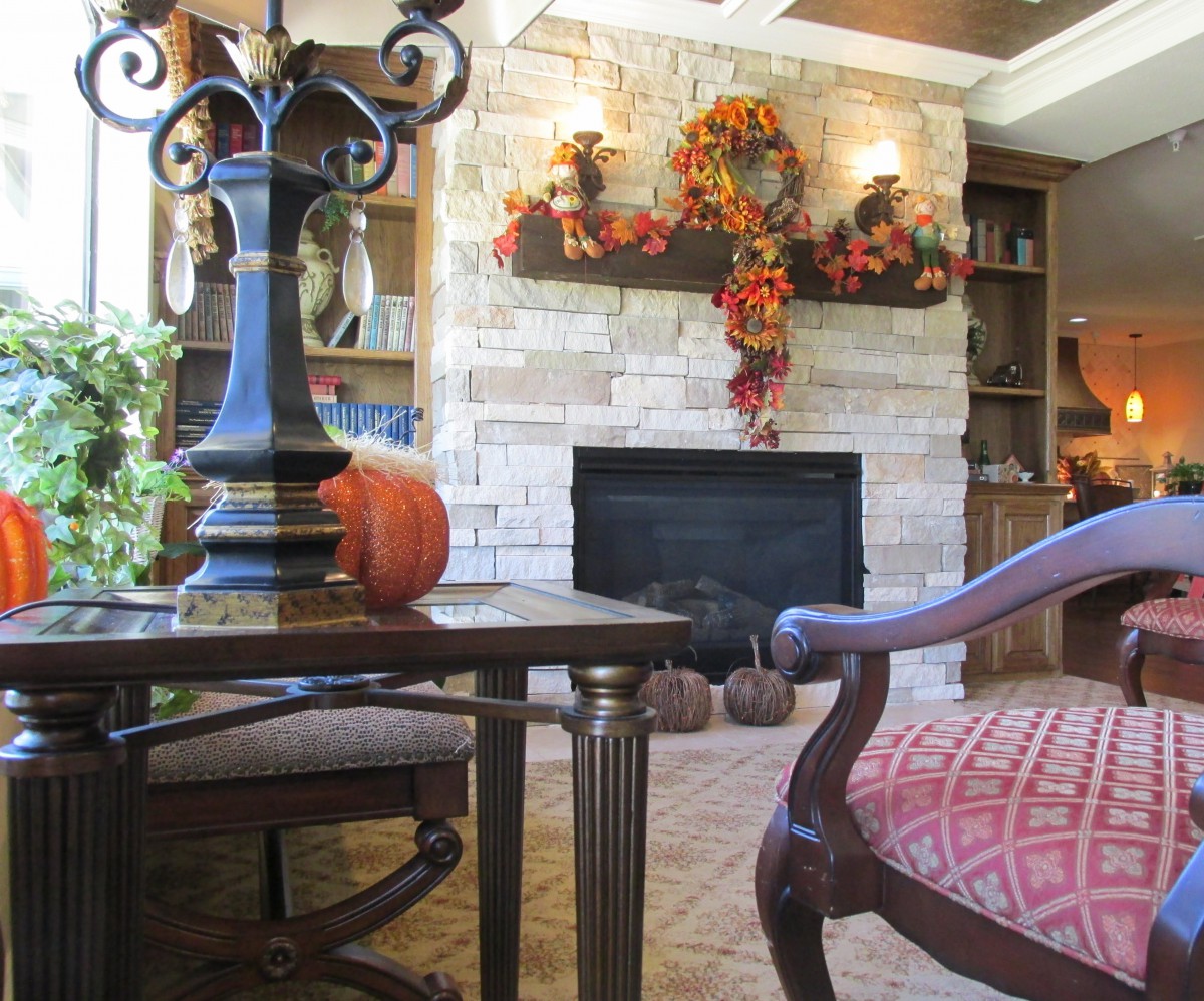 A cozy living room with autumn-themed decorations, featuring a fireplace and a pumpkin on the table.