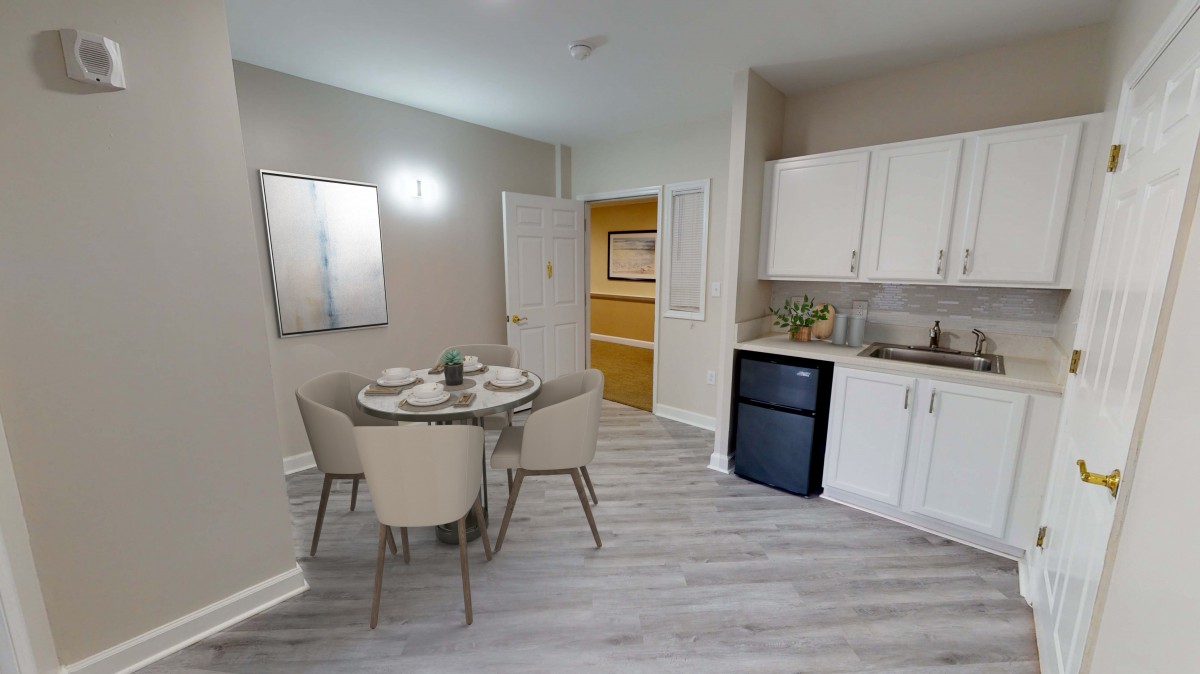A modern dining area with a round table, chairs, and a small kitchenette.