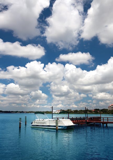 A serene view of a boat docked at a pier under a sky filled with fluffy clouds.