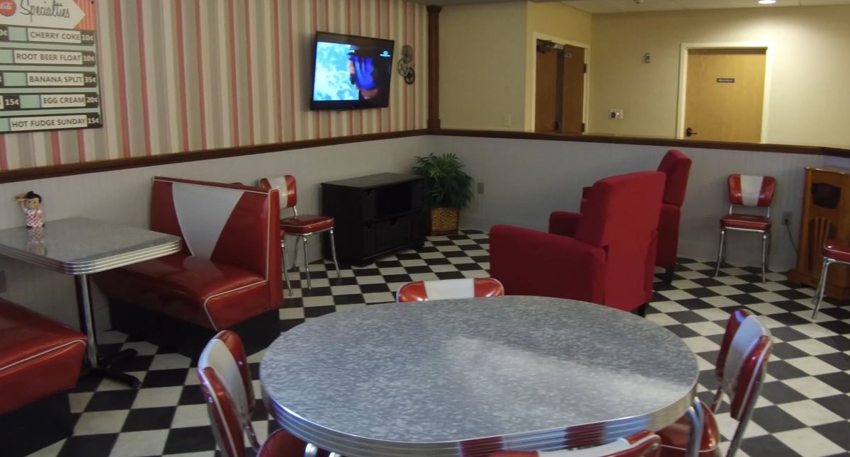 A retro-style diner interior with red seating and a checkerboard floor.