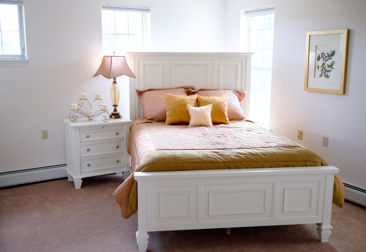 A cozy bedroom with white furniture and warm-toned bedding.