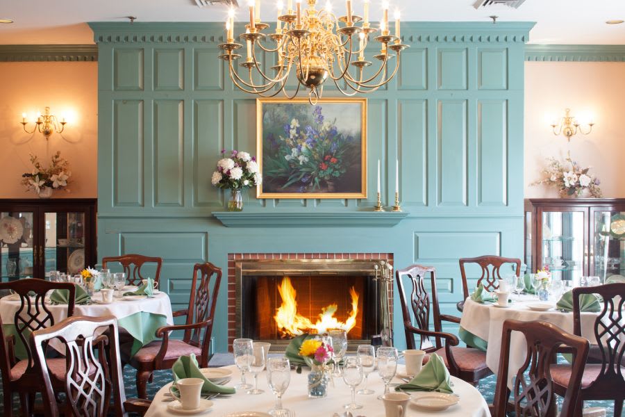 A formal dining room featuring a lit fireplace, an ornate chandelier, and elegantly set tables.
