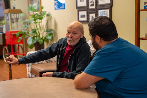 An elderly man engages in a thoughtful conversation with a caregiver in a cozy indoor setting.