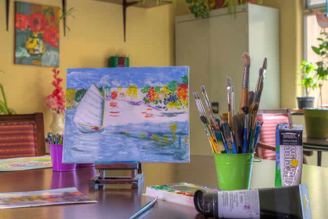 A colorful painting on a canvas sits on an easel, surrounded by brushes and art supplies in a creative workspace.