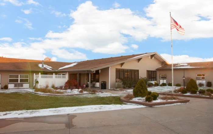 A suburban house with a brown roof and snow scattered on the lawn under a cloudy sky.