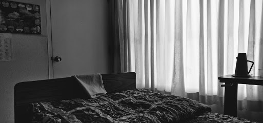 A serene black and white depiction of a bedroom with soft curtains filtering light.