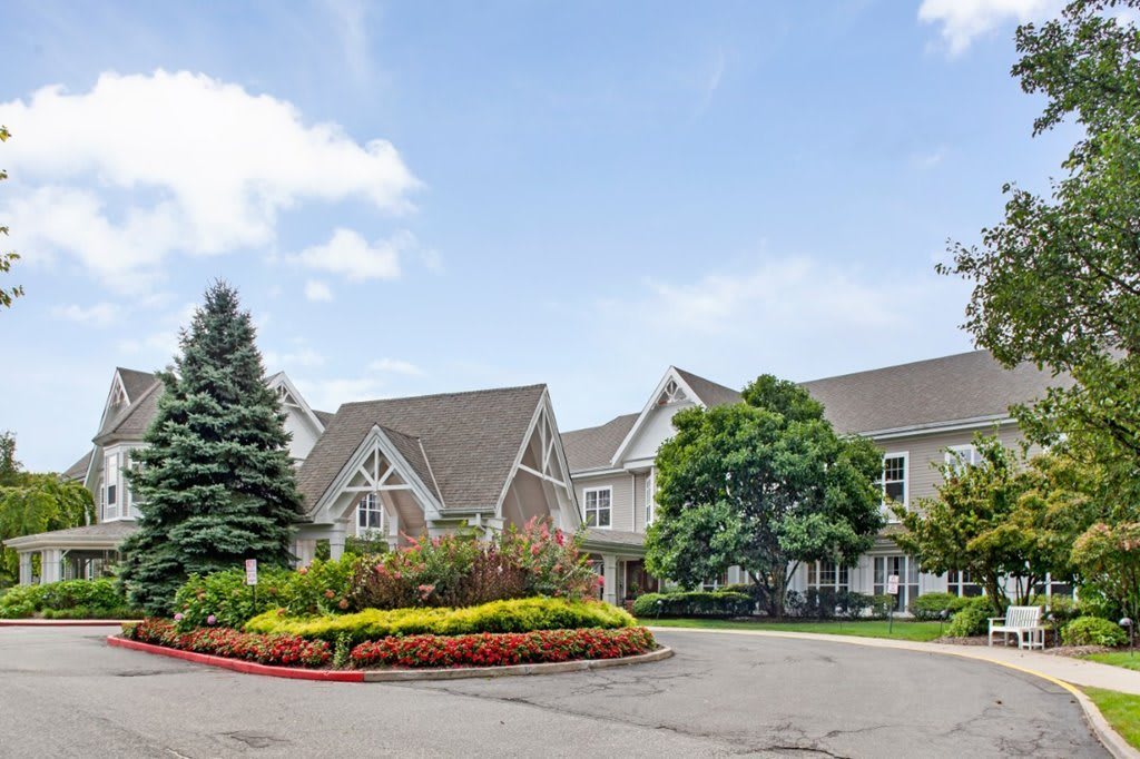 A suburban house with a driveway surrounded by trees and flowers.