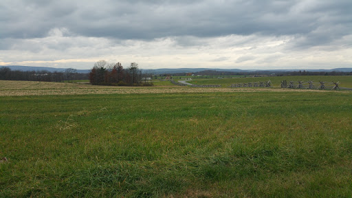 A serene view of a grassy field under a cloudy sky, stretching toward the distant hills.