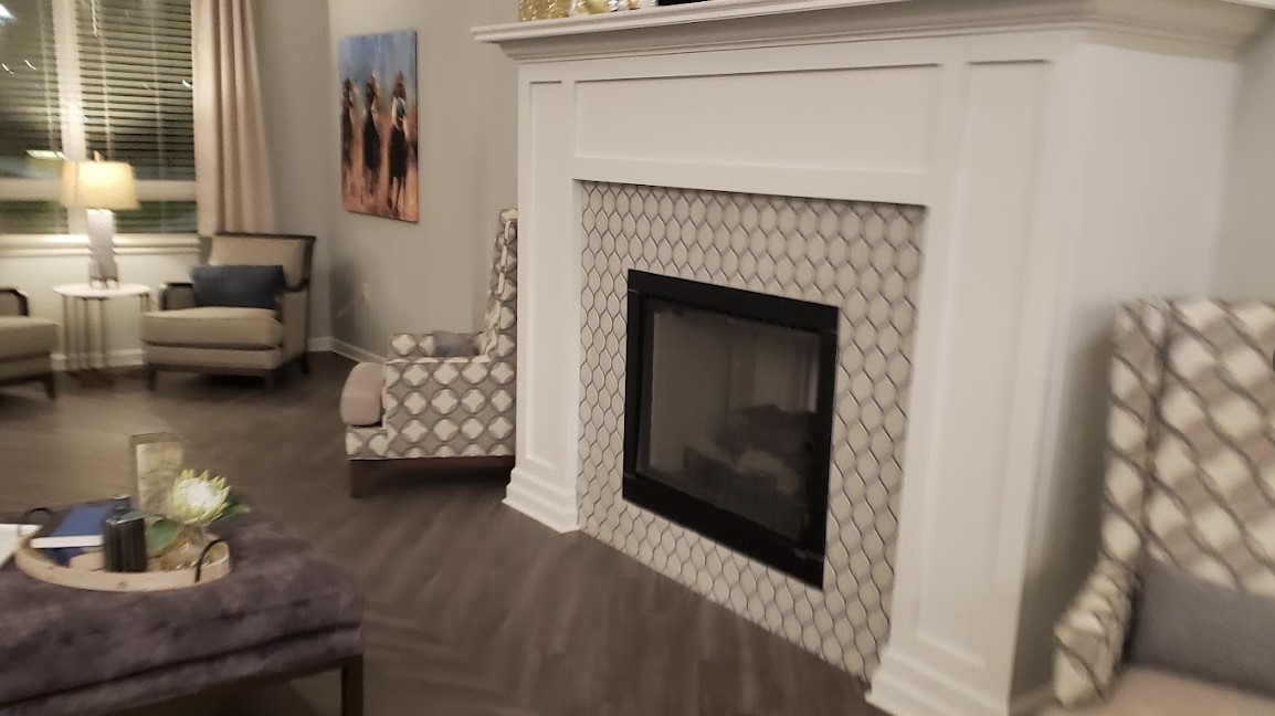 A modern living room features a stylish fireplace with a patterned tile surround, accompanied by a patterned chair and wall artwork.