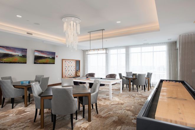 A modern dining area with elegant furnishings, featuring a chandelier and ample natural light.