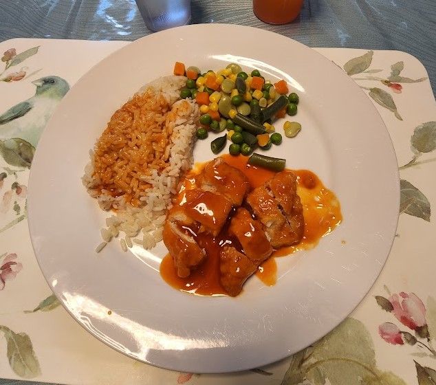 A plate of food featuring rice, mixed vegetables, and saucy meat.