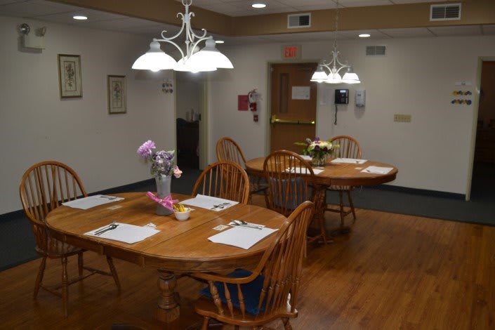 A well-lit dining area with wooden tables and chairs, adorned with flower centerpieces.