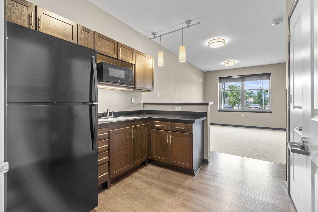 A modern kitchen with wooden cabinets and black appliances in an open floor plan apartment.