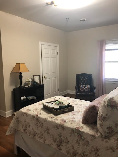A cozy bedroom with a bed, side table, lamp, chair, and window.