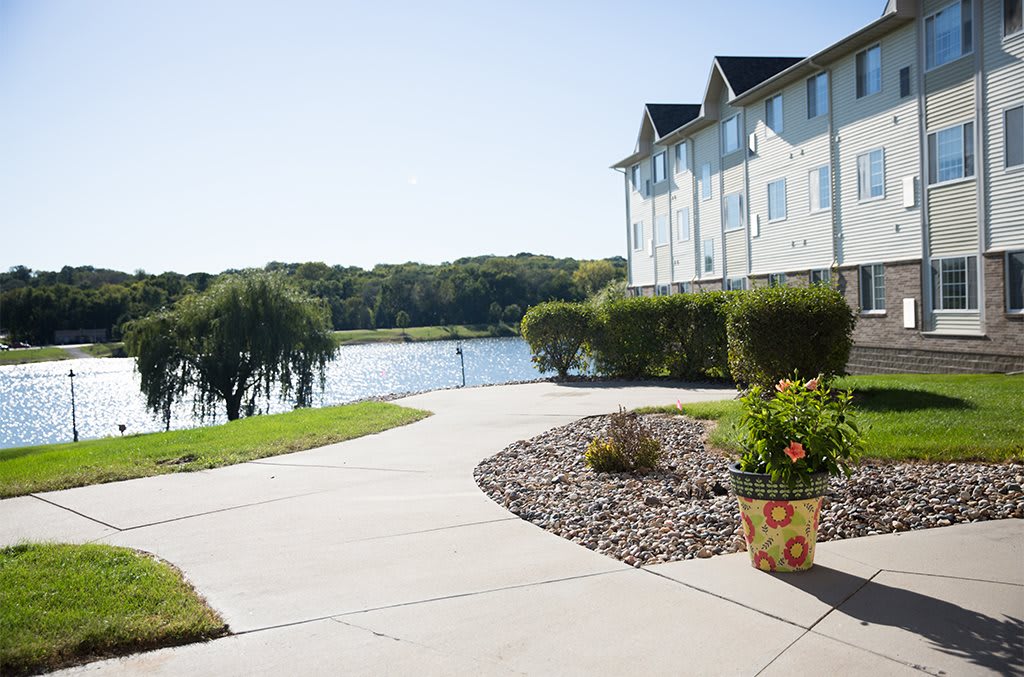 A sunny view of a lakeside apartment with a landscaped sidewalk and blooming flowers.
