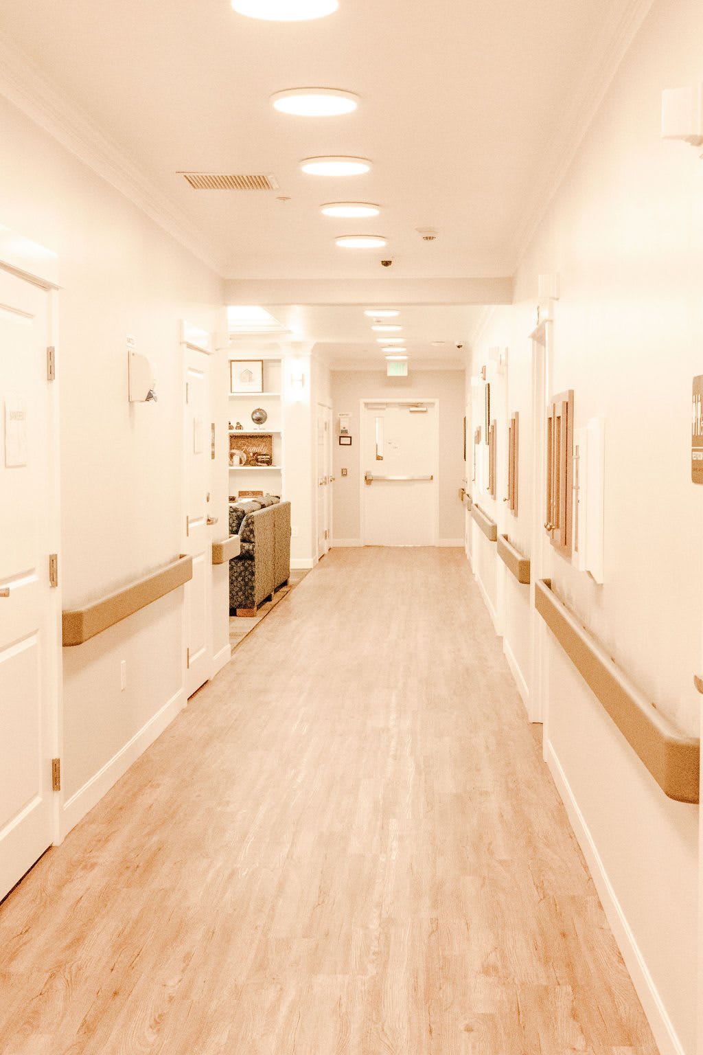 A bright and clean hospital corridor with wooden flooring and handrails.