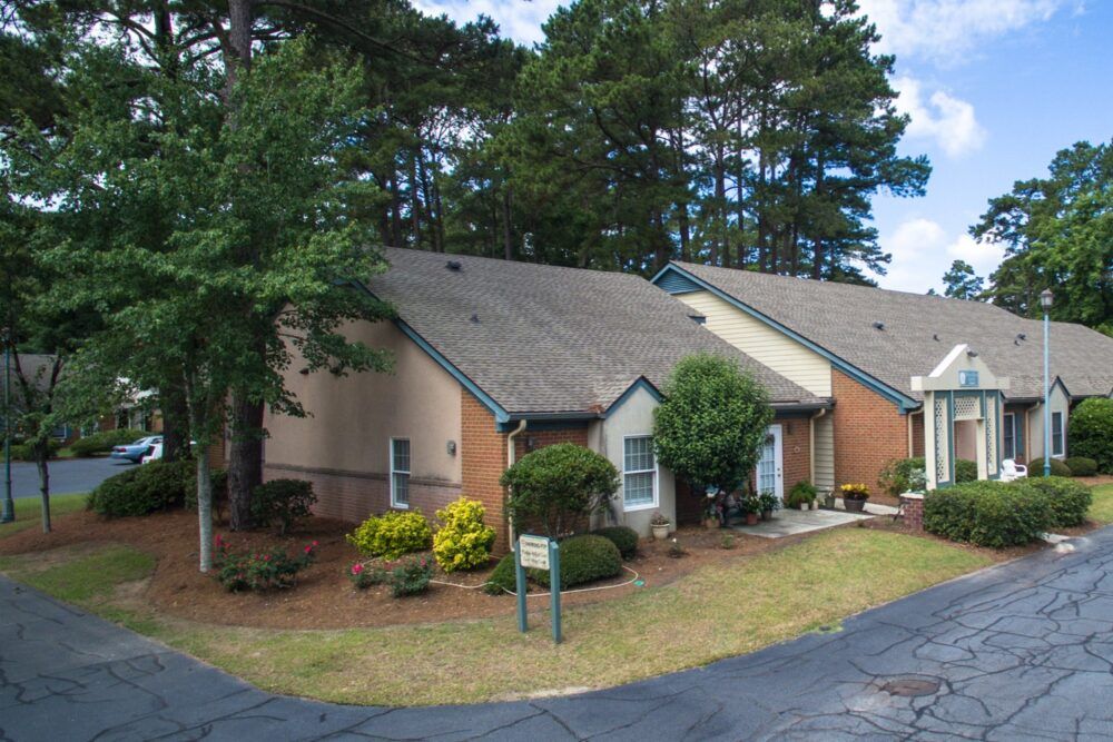 A suburban residential house with well-maintained landscaping and a driveway, surrounded by trees.