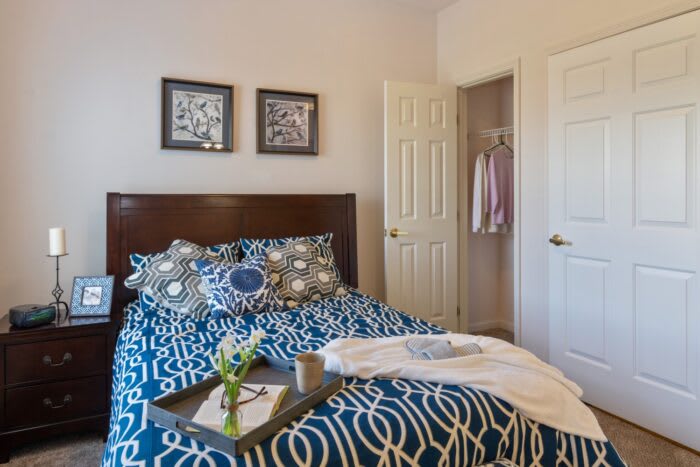 A cozy bedroom featuring a stylish bed with patterned bedding, decorative pillows, and wall art. A tray sits on the bed with a vase of flowers.