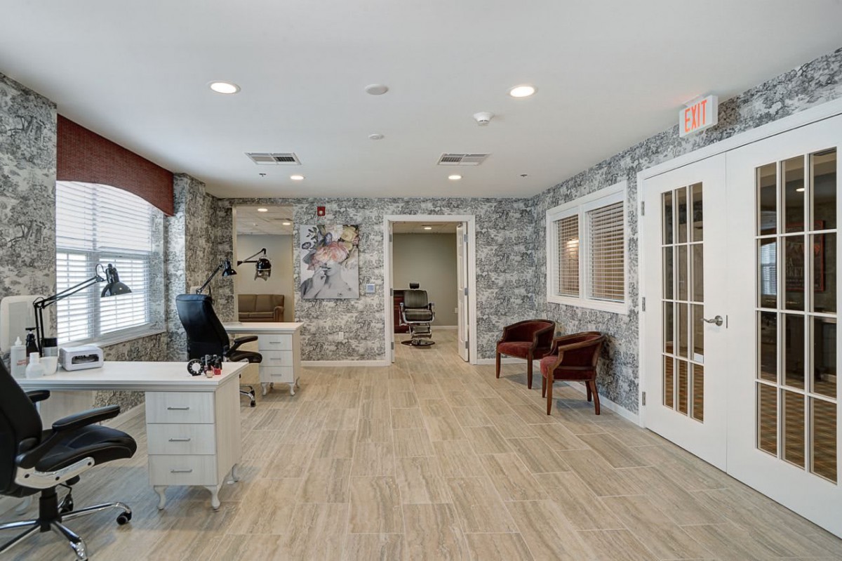 A modern office interior with a desk, chairs, wood flooring, and patterned wallpaper.