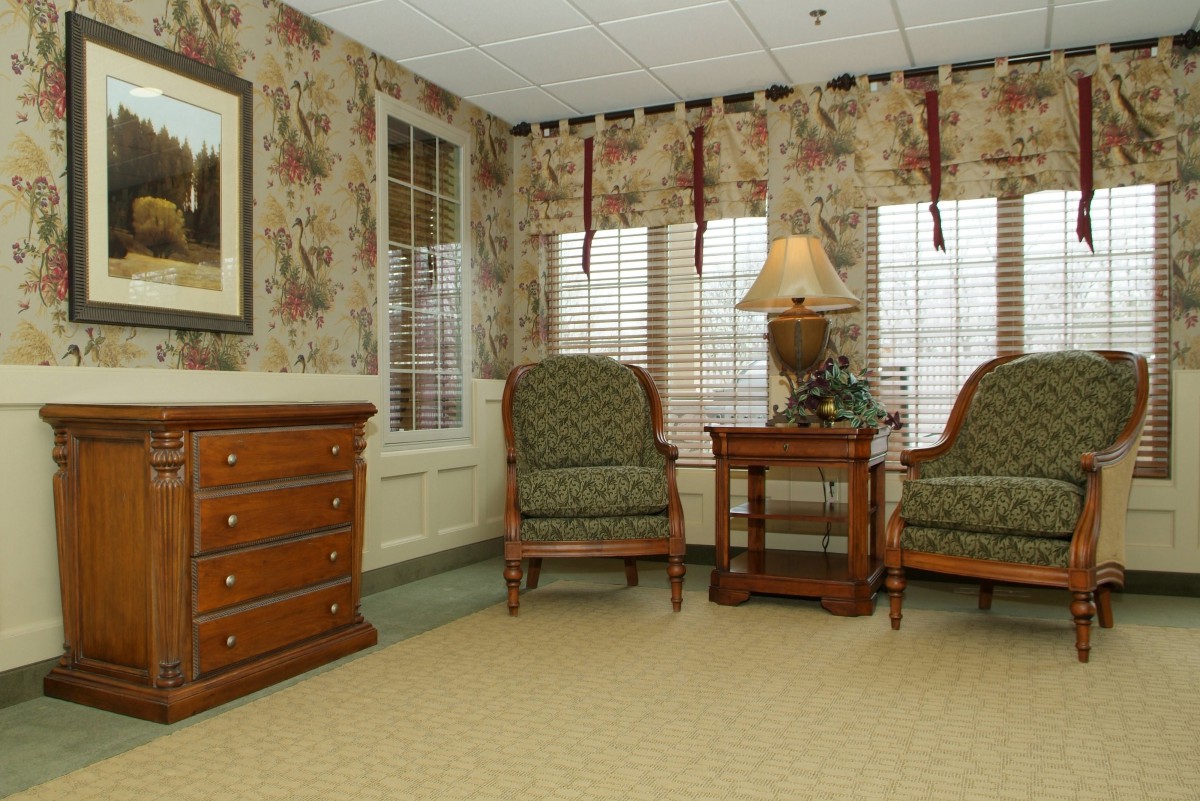A cozy living room with patterned armchairs, a wooden side table, and a lamp by the window.