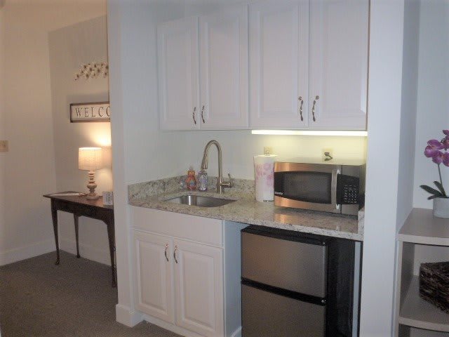 A compact kitchenette with white cabinets, a sink, microwave, and mini fridge.
