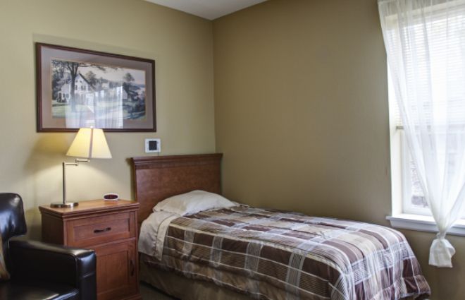 A cozy bedroom with a single bed, wooden nightstand, and a lamp, featuring wall art.