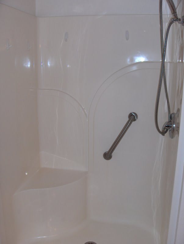 A bathroom shower with a grab bar and handheld showerhead.