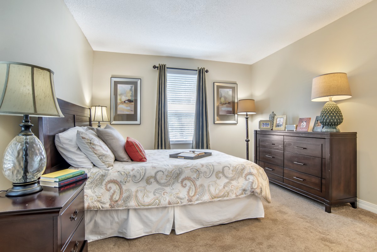 A cozy bedroom with a neatly made bed, dresser, and warm lighting.