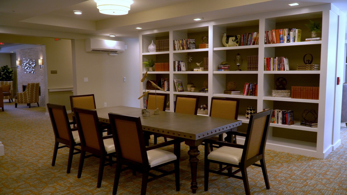 A well-lit conference room with a large table surrounded by chairs, and bookshelves in the background.