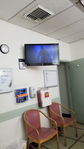 A view of a hospital waiting room featuring a wall-mounted TV, chairs, and a clock.