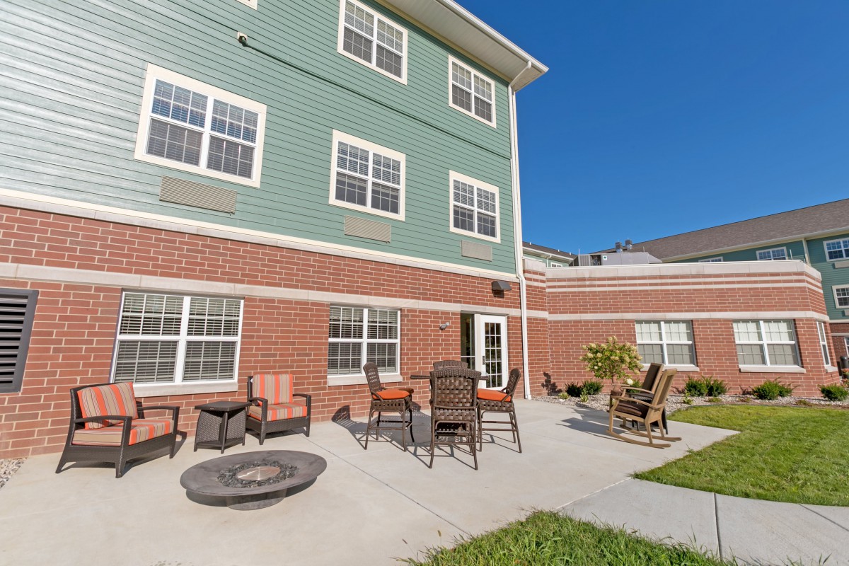 A sunny outdoor patio area with chairs and a fire pit in front of a multi-story building.