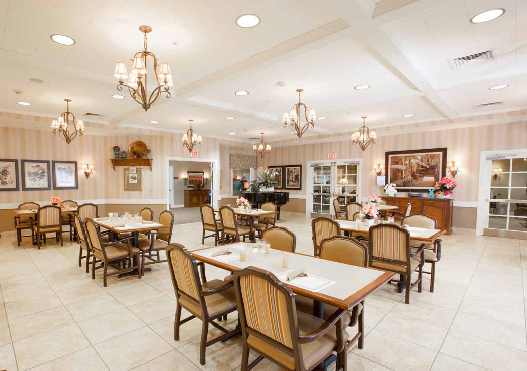 A well-lit dining area with arranged tables and chairs, featuring elegant chandeliers.