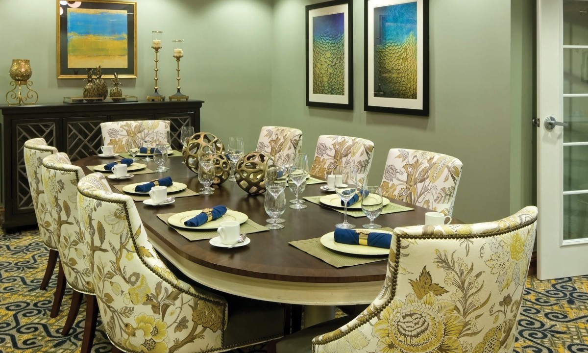 An elegantly arranged dining room with a beautifully set table, featuring floral upholstered chairs and framed artwork on the walls.