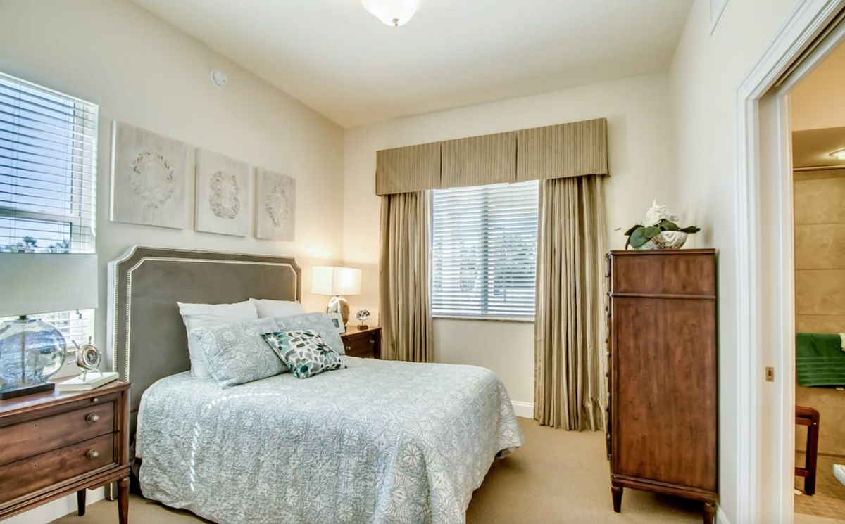 A cozy bedroom with neutral colors, featuring a comfortable bed, elegant curtains, and simple decor.