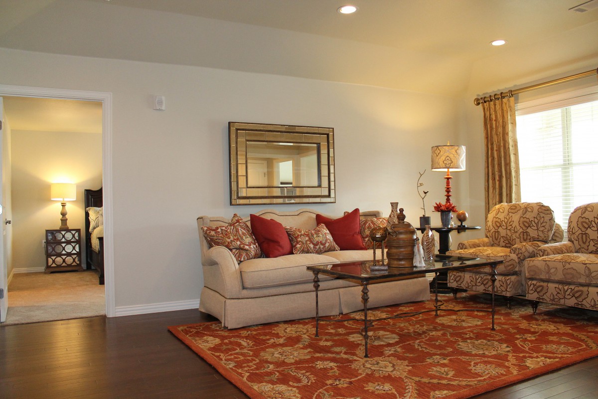 A cozy living room featuring a beige sofa with red and patterned pillows, a glass coffee table, a decorative rug, and a wall mirror.