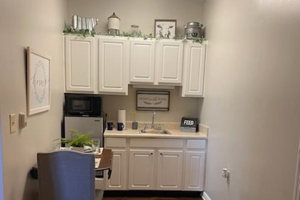 A cozy kitchenette with white cabinets, a mini fridge, and decorative elements.