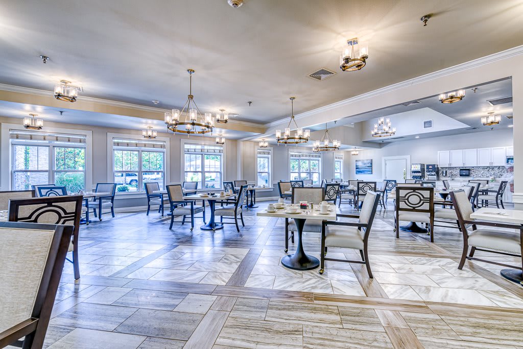 A spacious dining area with elegant chandeliers, featuring neatly arranged tables and chairs on wooden flooring.