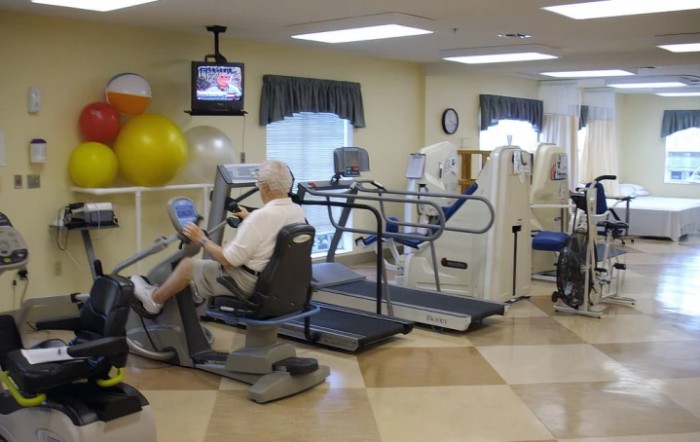 A senior person exercising in a rehabilitation facility equipped with various fitness machines.