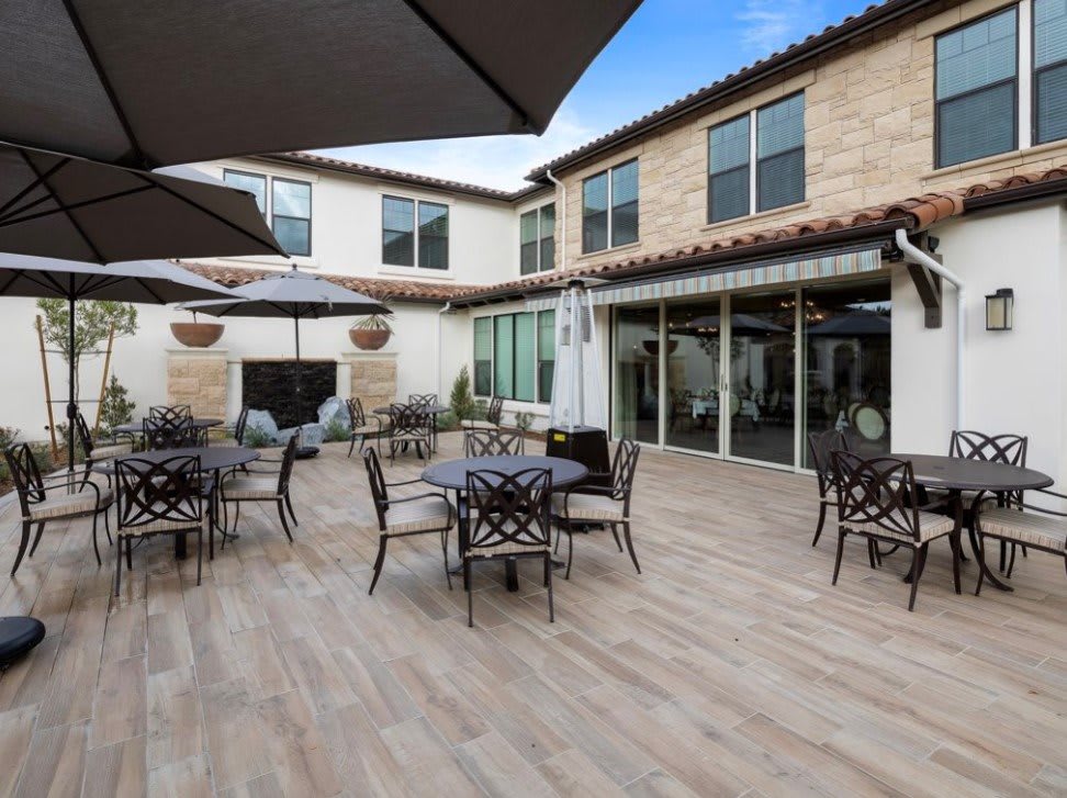 A spacious outdoor patio area with tables, chairs, and umbrellas in front of a modern building.