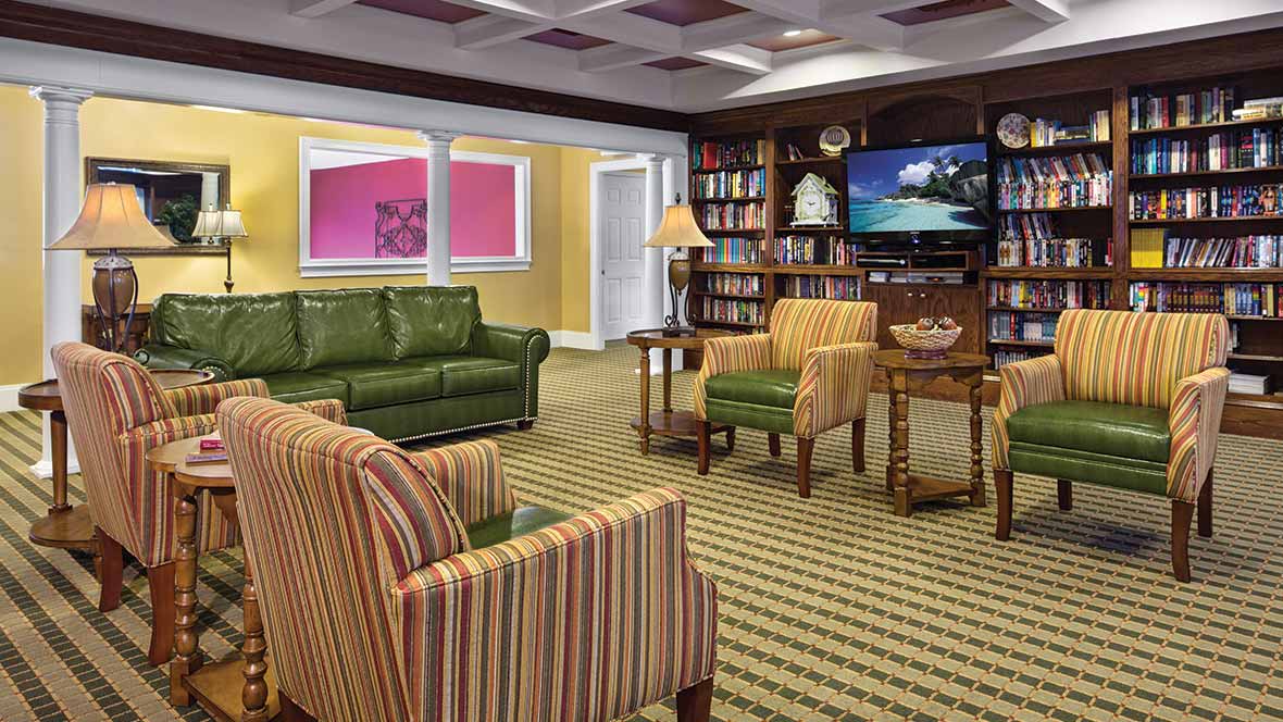 A cozy living room with a green sofa, striped chairs, bookshelves, and a TV.
