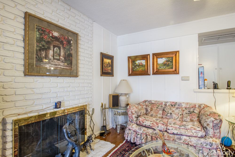 A cozy living room with a brick fireplace, floral couch, and framed paintings on the wall.
