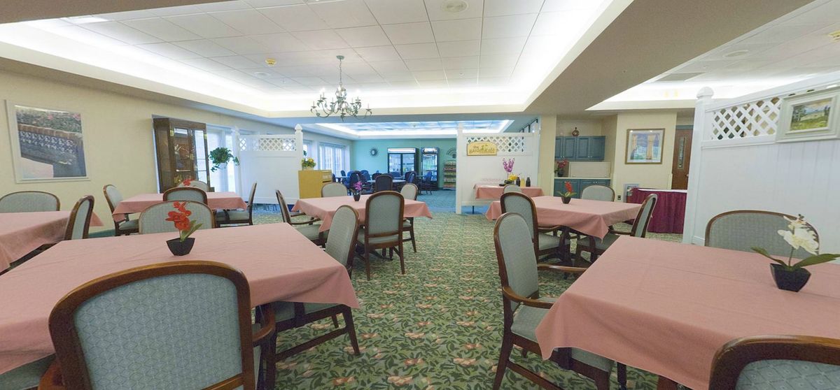 A spacious dining room with neatly arranged tables and chairs, featuring a chandelier and patterned carpet.