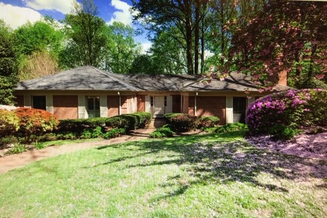 A suburban brick house surrounded by greenery and trees on a sunny day.