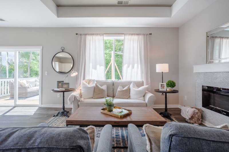 A modern living room with neutral tones, featuring a comfortable sofa, coffee table, and stylish decor, illuminated by natural light through a large window.