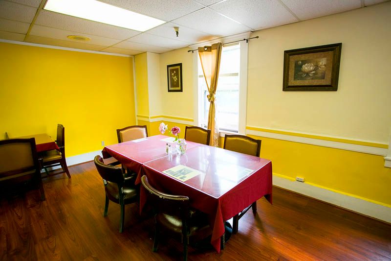 A cozy dining room with yellow walls, a table covered with a red tablecloth, and several chairs.